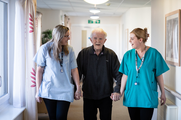 resident walking hand in hand with care givers