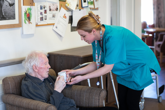 care worker wearing green uniform handing a cup of tea to resident